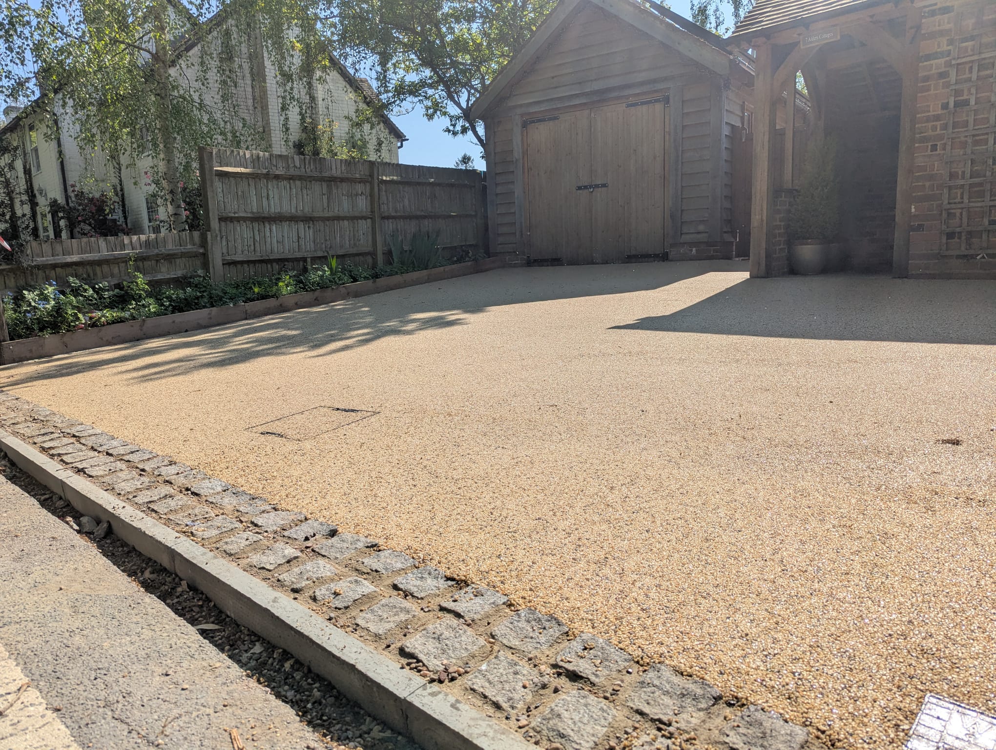 Golden resin-bound driveway with granite sett edging outside a barn-style garage