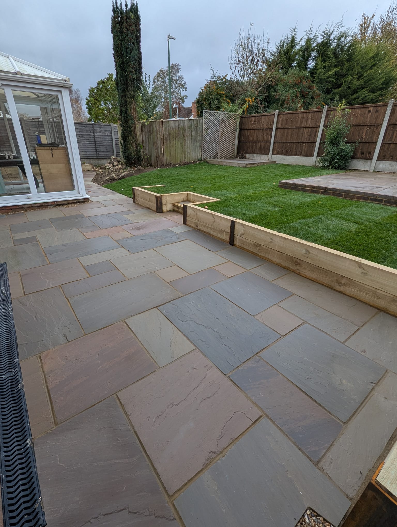 Indian sandstone terrace with oak sleeper raised beds and new turf lawn